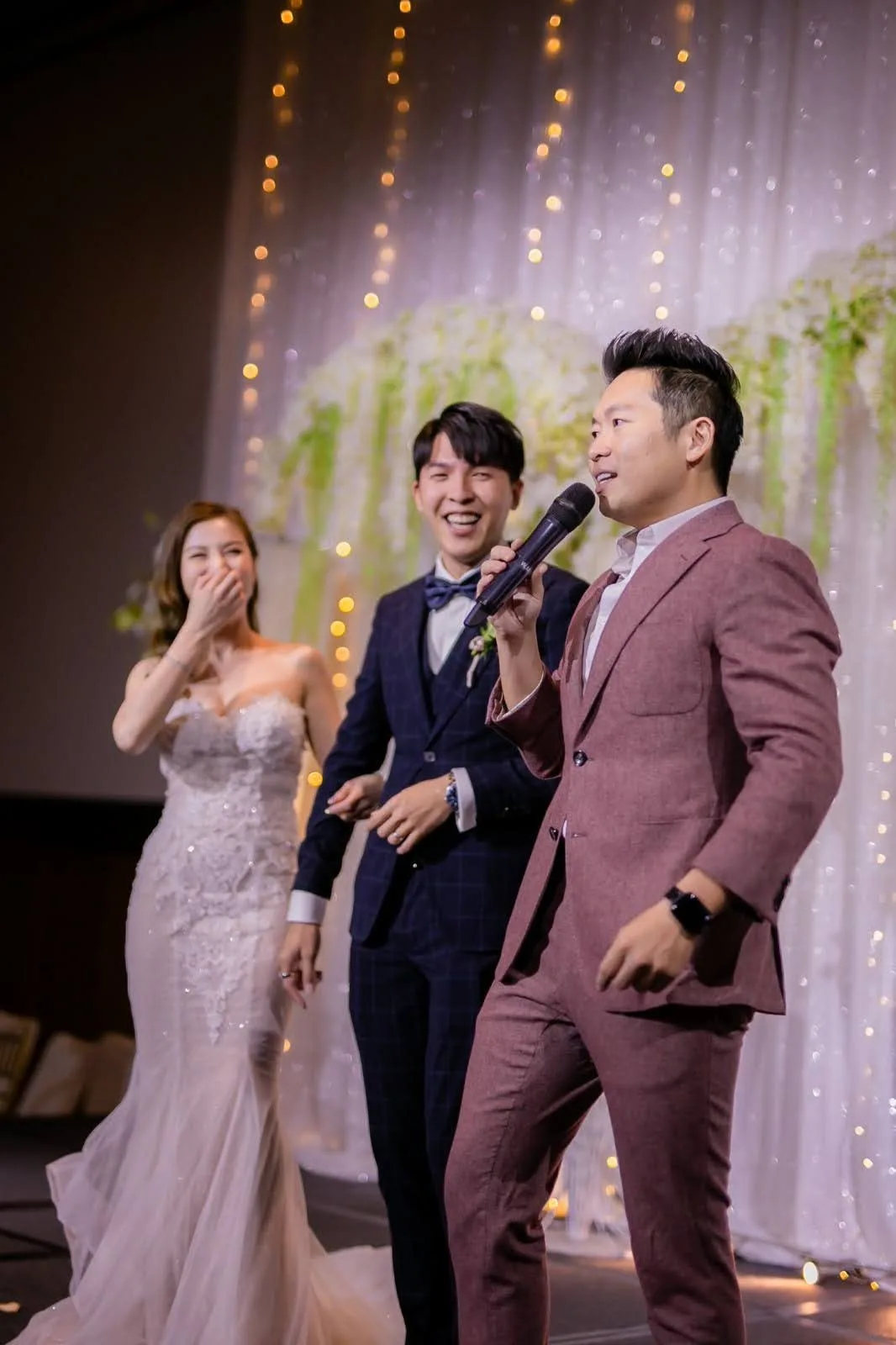 James Yang with the bride and groom on stage at a wedding banquet