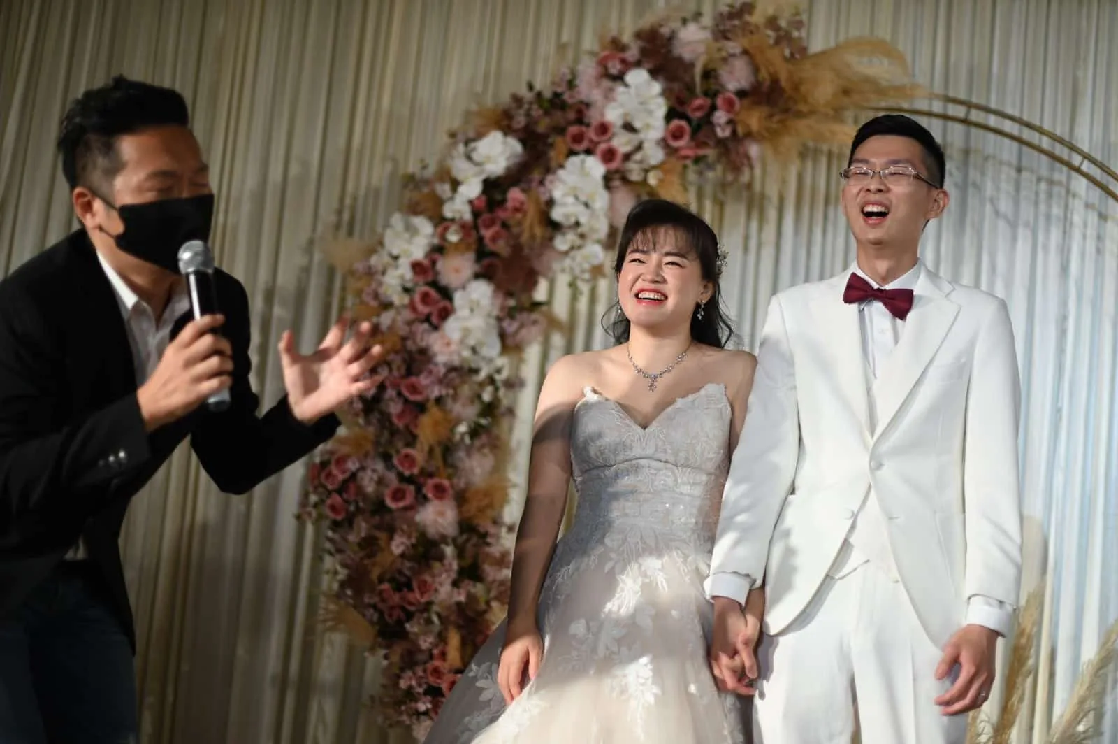 James Yang with the bride and groom under a floral arch at a wedding banquet
