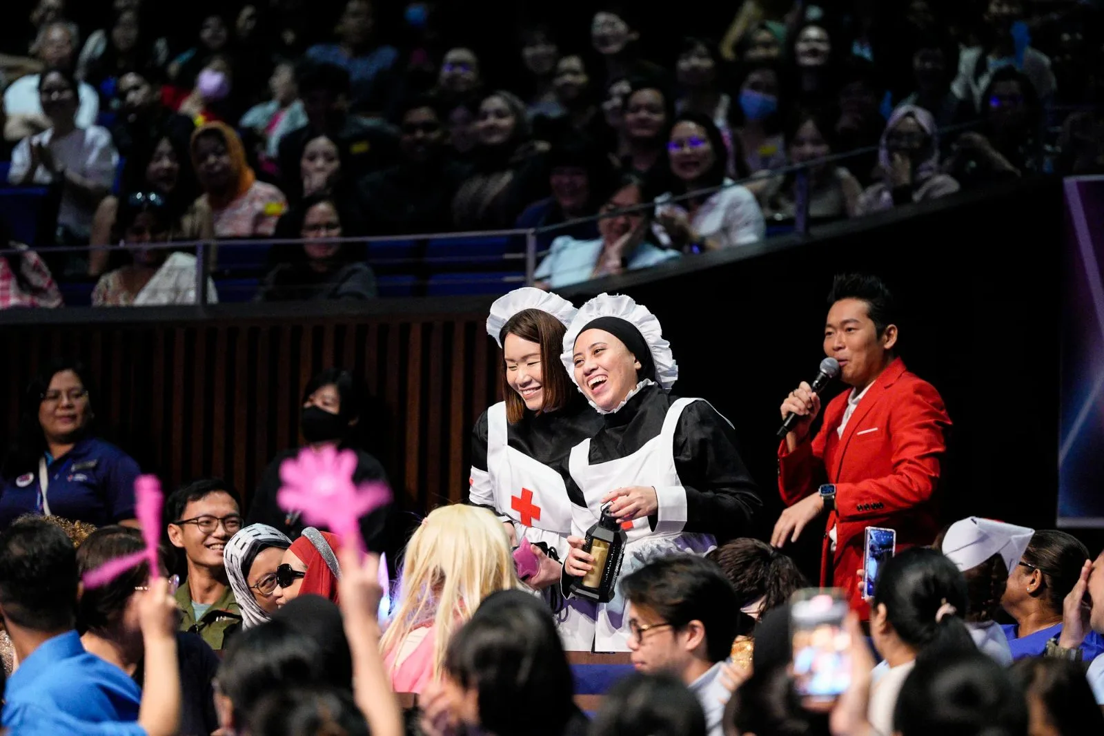 James Yang in a red suit on stage with performers in costume, the audience cheering