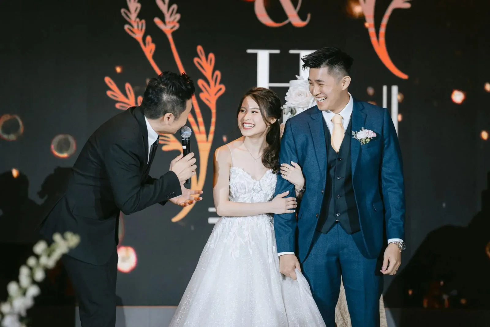 James Yang with the bride and groom on stage at a wedding banquet