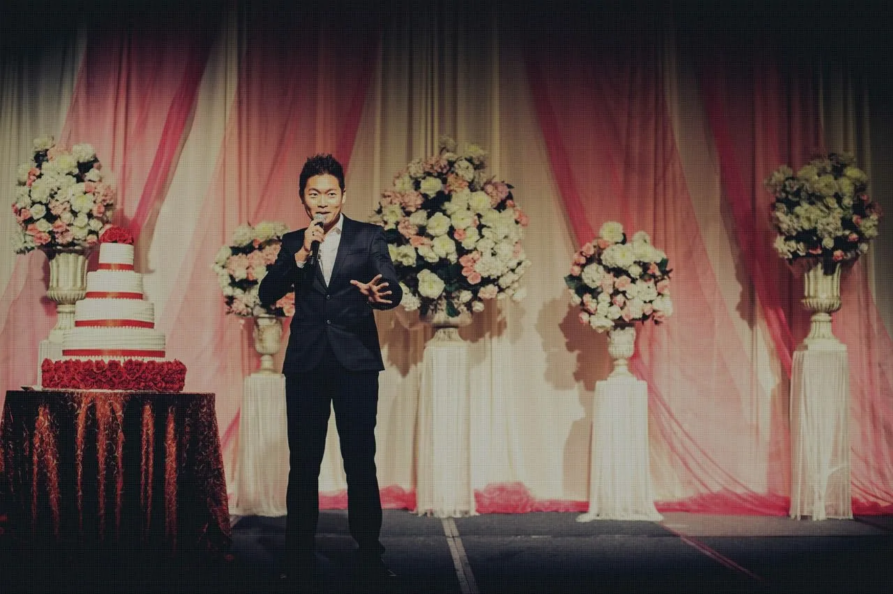James Yang hosting a wedding banquet beside the wedding cake and floral arch